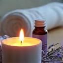Vela aromática encendida y aceites esenciales junto a una toalla de spa y flores de lavanda.